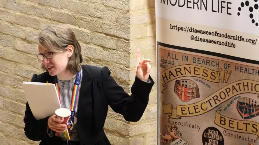 Dr Catherine Charlwood stands in front of the Diseases of Modern Life Banner